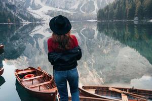wunderschönes Stück Natur. Frau mit schwarzem Hut genießt majestätische Berglandschaft in der Nähe des Sees mit Booten