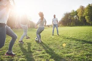 eine Gruppe von Freunden in legerem Outfit spielt Fußball unter freiem Himmel. Leute haben Spaß und haben Spaß. aktive Erholung und malerischer Sonnenuntergang foto