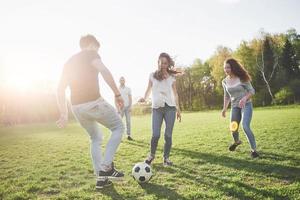 eine Gruppe von Freunden in legerem Outfit spielt Fußball unter freiem Himmel. Leute haben Spaß und haben Spaß. aktive Erholung und malerischer Sonnenuntergang foto