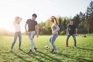 eine Gruppe von Freunden in legerem Outfit spielt Fußball unter freiem Himmel. Leute haben Spaß und haben Spaß. aktive Erholung und malerischer Sonnenuntergang foto
