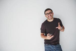 junger glücklicher Mann lässig gekleidet mit Smartphone auf weißem Hintergrund
