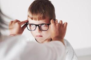 lustiges Kind. Arzt gibt dem Kind eine neue schwarze Brille für seine Vision foto