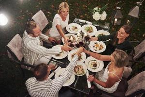 viel glück für alle. Ansicht von oben. Gruppe von Freunden in der eleganten Kleidung haben ein luxuriöses Abendessen foto