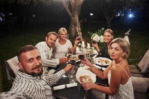 Kerl macht Selfie. Gruppe von Freunden in der eleganten Kleidung haben ein luxuriöses Abendessen foto