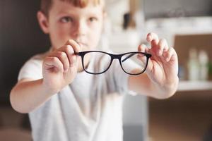 kleiner Junge hält seine neue Brille in der Arztpraxis foto