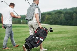 Rückansicht. zwei Freunde, die mit Golfausrüstung durch den Rasen laufen und sich unterhalten foto