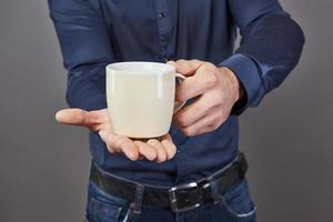 Gut aussehender bärtiger Mann mit stylischem Haarbart und Schnurrbart auf ernstem Gesicht im Hemd, das weiße Tasse oder Tasse hält, die Tee oder Kaffee im Studio auf grauem Hintergrund trinkt foto