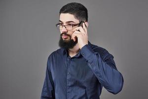 glücklicher Mann mit Brille spricht telefonisch auf grauem Hintergrund
