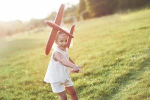 in die Luft starten. glückliches kleines Mädchen, das mit rotem Spielzeugflugzeug in den Händen auf dem Feld läuft foto