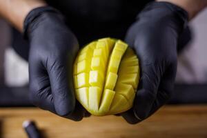 Person mit schwarz Handschuhe Schneiden und Schneiden Mango zum Smoothie Holz Schneiden foto