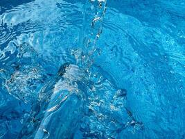 dynamisch Spritzen im Kristall klar Blau Wasser und Glas Flasche, Erstellen Wellen und Wasser Tröpfchen im Bewegung. sauber Wasser Konzept. foto