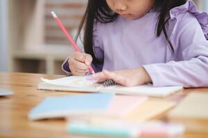 ein jung Mädchen ist Schreiben mit ein rot Bleistift auf ein Stück von Papier foto