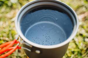 Tourist Utensilien zum Kochen im Natur, ein Topf von Wasser kocht auf das Brenner, Luft Luftblasen erhebt euch zu das Oberfläche von das Wasser, warm das Tee. foto