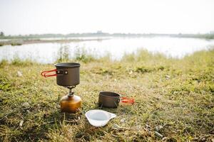 Camping im Natur durch das Fluss, das Konzept von ein Tourist Küche auf ein Wanderung, ein einstellen von Platten mit Griffe, Geschirr zum Kochen auf ein Gas Brenner auf ein Wanderung. foto