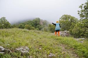 Reisen im das Berge nebelig Wetter, das Kerl Punkte das Weg mit seine Hand, das Aussicht hinter das Tourist mit ein Rucksack, ein Solo Reise, ein extrem Wanderung im das Wald. foto