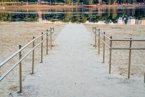 Abstammung zu das Wasser zum das deaktiviert im ein Rollstuhl, ein ausgestattet Pfad mit Handläufe, ein Stadt Strand auf das See, ein Weiß Sand Teich, fein Sand Nein Personen. foto