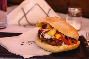 Hamburger Besondere mit Rindfleisch oder Hähnchen Burger, mit Tomate, Ketchup, Senf, Käse, Speck, Zwiebel, Tzatziki und Kartoffeln serviert auf schwarz Teller im griechisch Taverne. selektiv Sanft Fokus foto