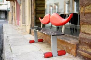 Chios, Griechenland Dezember 07 2023. kreativ Bank gemacht von Skateboard mit groß Holz rot Schnurrbart Elemente im Hippie Stil. modern städtisch Straße Möbel. mit Nein Menschen foto