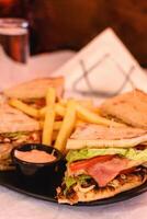 Vertikale Aussicht von Verein Pita-Brot Giro Hähnchen mit Käse, Speck, Tomate, Kopfsalat, Soße serviert mit Fritten auf das schwarz Teller auf Weiß Tischdecke im griechisch Taverne. Tabelle Einstellung. selektiv Sanft Fokus foto