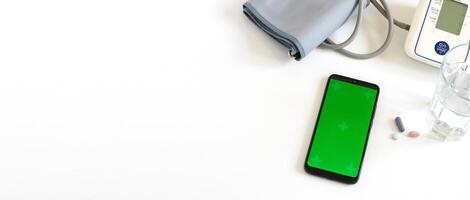 Smartphone mit Chroma Schlüssel Bildschirm auf das Weiß Hintergrund mit automatisch Blut Druck Monitor, Pillen, ein Glas von Wasser. Gesundheit und medizinisch Konzept. Banner. Kopieren Raum foto