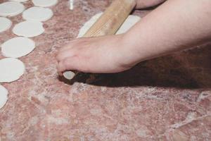 Eine Frau rollt den Teig mit einem hölzernen Nudelholz auf einer Küchenarbeitsplatte aus Marmor aus. foto