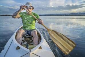 Senior männlich Paddler Paddeln ein geschmückt Expedition Kanu mit ein Wasser Spritzen auf ein See im Nord Colorado foto