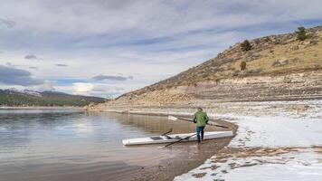 Senior männlich Ruderer mit ein Küsten Rudern Schale und Beil Ruder auf ein Ufer von Fuhrmann See im fallen oder Winter Landschaft im Nord Colorado. foto