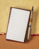 leer Blatt von regiert Papier im ein klein Tagebuch mit ein Luxus Stift gegen texturiert Kunst Papier foto