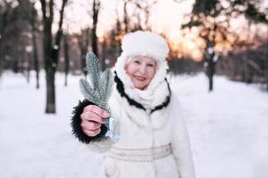 ältere Frau in weißem Hut und Pelzmantel, die den Winter im Schneewald genießt. Winter, Alter, Saisonkonzept