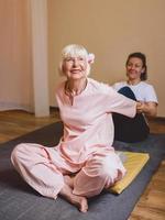 Senior kaukasische stilvolle Frau mit grauem Haar und rosa Phalaenopsis in ihrem Haar, die bei thailändischer Massage sitzt. Anti-Age, gesunder Lebensstil, Reisen, Thai-Massage-Konzept foto