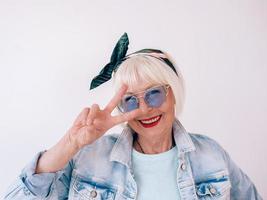 Senior stilvolle Frau mit grauem Haar mit modischem Stirnband und blauer Brille. Mode, Anti-Age, Entspannung, Urlaub, Ruhestandskonzept foto