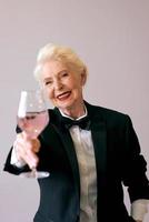 stilvolle reife Sommelier-Senior-Frau im Smoking mit einem Glas Wein. Spaß, Party, Stil, Lifestyle, Arbeit, Alkohol, Feierkonzept foto