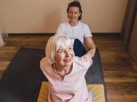 Senior kaukasische stilvolle Frau mit grauem Haar und rosa Phalaenopsis in ihrem Haar, die bei thailändischer Massage sitzt. Anti-Age, gesunder Lebensstil, Reisen, Thai-Massage-Konzept foto