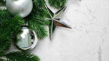 Grüne Kiefernblätter auf weißem Marmorhintergrund, Weihnachtsdekorationen in heller silberner Farbe. einfaches und kreatives Weihnachtskonzept. foto
