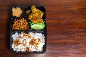 indonesisch Mahlzeit Box namens uduk platziert auf das hölzern Tisch. nach etwas bearbeitet. foto