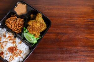 indonesisch Mahlzeit Box namens uduk platziert auf das hölzern Tisch. nach etwas bearbeitet. foto