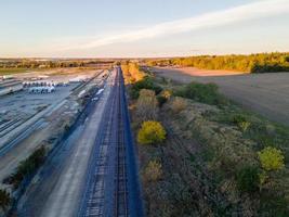 Luftaufnahme des landwirtschaftlichen Feldes und des Schienenverkehrs, die bei Sonnenuntergang verschmelzen foto