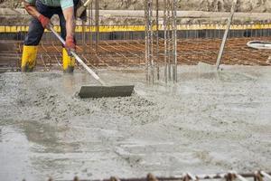 ein Maurer, der den frisch gegossenen Beton nivelliert, um das Fundament eines Gebäudes zu legen foto