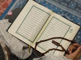 ein jung asiatisch Muslim Frau hält Gebet Perlen und liest das Koran beim ein Moschee während das Fasten Monat von Ramadan. foto