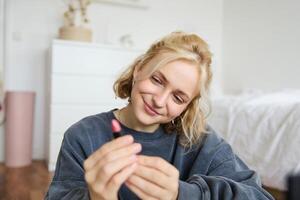 Porträt von lächelnd schön Frau im ihr Zimmer, Sitzung und zeigen Lippenstift, empfehlen Lieblings Schönheit Produkt, Inhalt Hersteller Aufzeichnung ein von Sie selber zum Sozial Medien Blog foto