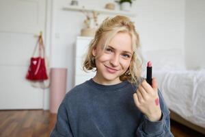 Porträt von lächelnd blond Frau, Aufzeichnung , online Leben Strom Über Schönheit Produkte, Inhalt Hersteller Preise ihr bilden Produkte, zeigt an Lippenstift auf Kamera foto