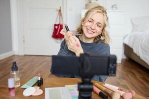 Porträt von jung kreativ Sozial Medien Inhalt Schöpfer, Frau zeigen Lippenstift Farbfelder auf ihr Hand, Aufzeichnung Über Schönheit und bilden, Sitzung im ihr Zimmer im Vorderseite von Digital Kamera foto
