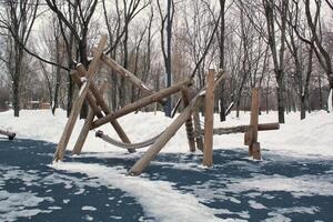 hölzern Spielplatz gemacht von natürlich umweltfreundlich Material im Öffentlichkeit Stadt Park mit Schnee beim Winter Zeit. modern Sicherheit Kinder draussen Ausrüstung. Winter Aktivitäten. Kinder sich ausruhen und Spiele auf öffnen Luft foto