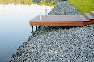 Boot Dock im das Stadt Park, das Stein Bank von das Fluss ist bedeckt mit Schutt, ein hölzern Seebrücke steht auf Stelzen, ein Platz zu entspannen durch das Wasser, ein ländlich Teich foto