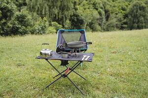 komfortabel Camping Möbel von kompakt Größe, ein Platz zu entspannen im Natur, ein Stuhl und ein Tisch, falten Elemente von Ausrüstung auf ein Wanderung, Geschirr auf das Tisch. foto