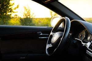 Lenkung Rad und Innere von modern Luxus Auto während Sonnenuntergang auf Autobahn Straße. Einzelheiten von Multimedia Speisekarte Steuerung System Tafel, Instrumententafel innen. Prestige Sport Automobil. selektiv Fokus foto