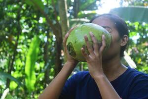 Tasikmalaya, ts, 2023 - - ein Sundanesisch Frau Getränke Grün Kokosnuss Wasser im ein Dorf im Tasikmalaya, Westen Java foto