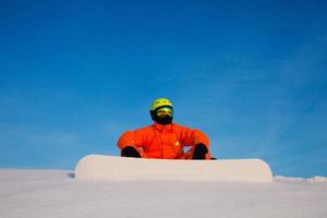 Snowboarder Freerider mit weißem Snowboard sitzt oben auf der Skipiste foto