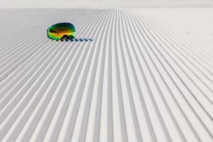 Skibrille, die auf einem neuen präparierten Schnee und einer leeren Skipiste liegt foto