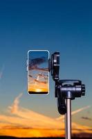 Smartphone auf Stativ zur Aufnahme des Sonnenuntergangs im vertikalen Modus foto